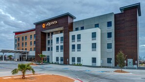 Un hotel moderno con un llamativo letrero de 'La Quinta', varios pisos y un estacionamiento con palmeras.