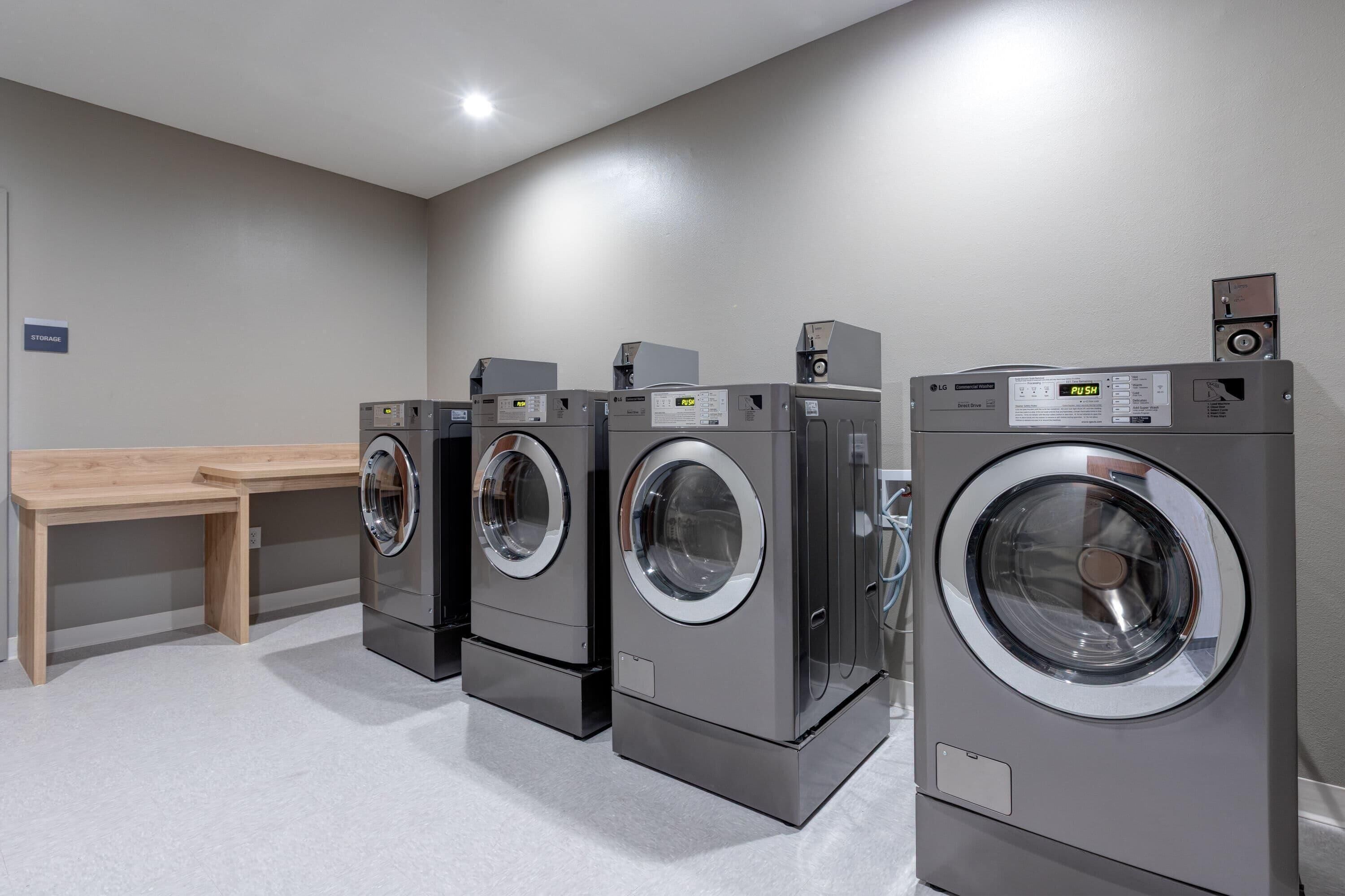 A laundry room with three front-loading washing machines and a wooden bench.