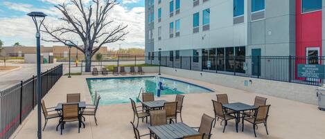 A hotel with a swimming pool, outdoor seating, and a modern building facade.