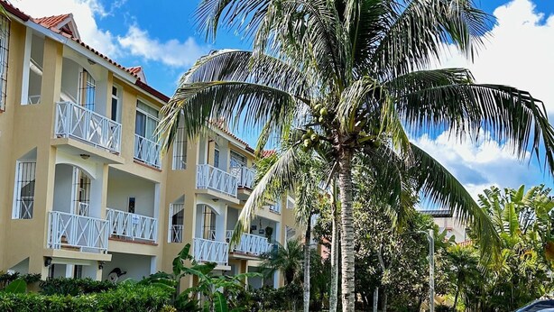 A hotel with a well-maintained garden, palm trees, and a clear blue sky.