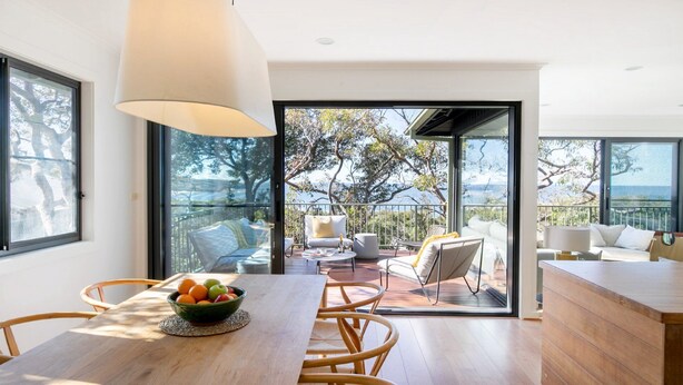 A modern dining area with a wooden table, chairs, and a bowl of fruit. - Great Views, Walk To Beach and Bay In Bush Setting (KILLCARE)