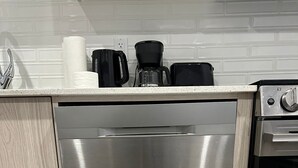 Ruostumattomasta teräksestä valmistettu astianpesukone ja uuni keittiössä, jossa on valkoinen työtaso ja puukaapit.