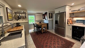 A modern kitchen with a stainless steel refrigerator, a wooden dining table, and a red patterned rug.