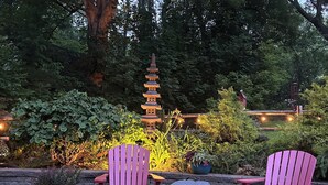 Two Adirondack chairs facing each other with a stone wall and a pagoda-style structure in the background.