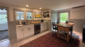 A kitchen with white cabinets, a wooden table, and a red patterned rug.