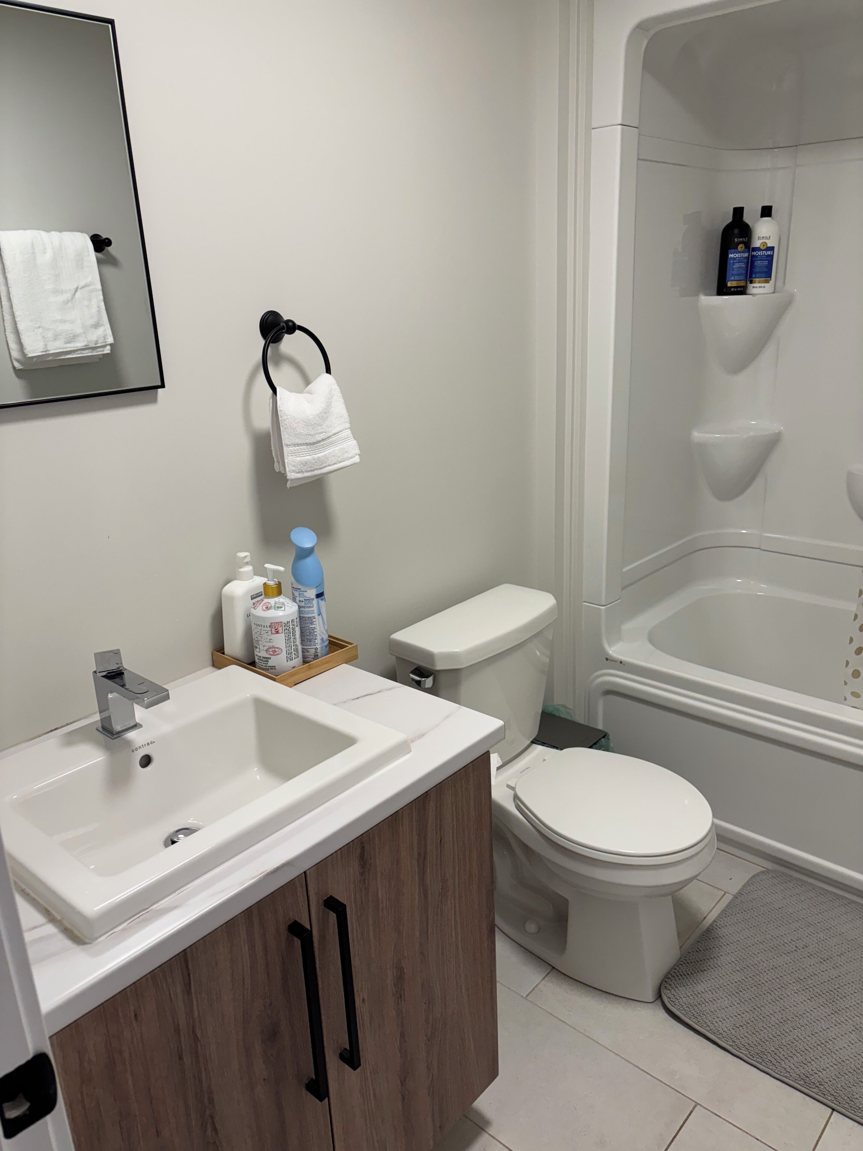 Ein Badezimmer mit einem weißen Waschbecken, einer Toilette und einer Badewanne. Auf dem Waschbecken stehen Pflegeprodukte und ein Handtuch hängt an einem Ablagegestell.