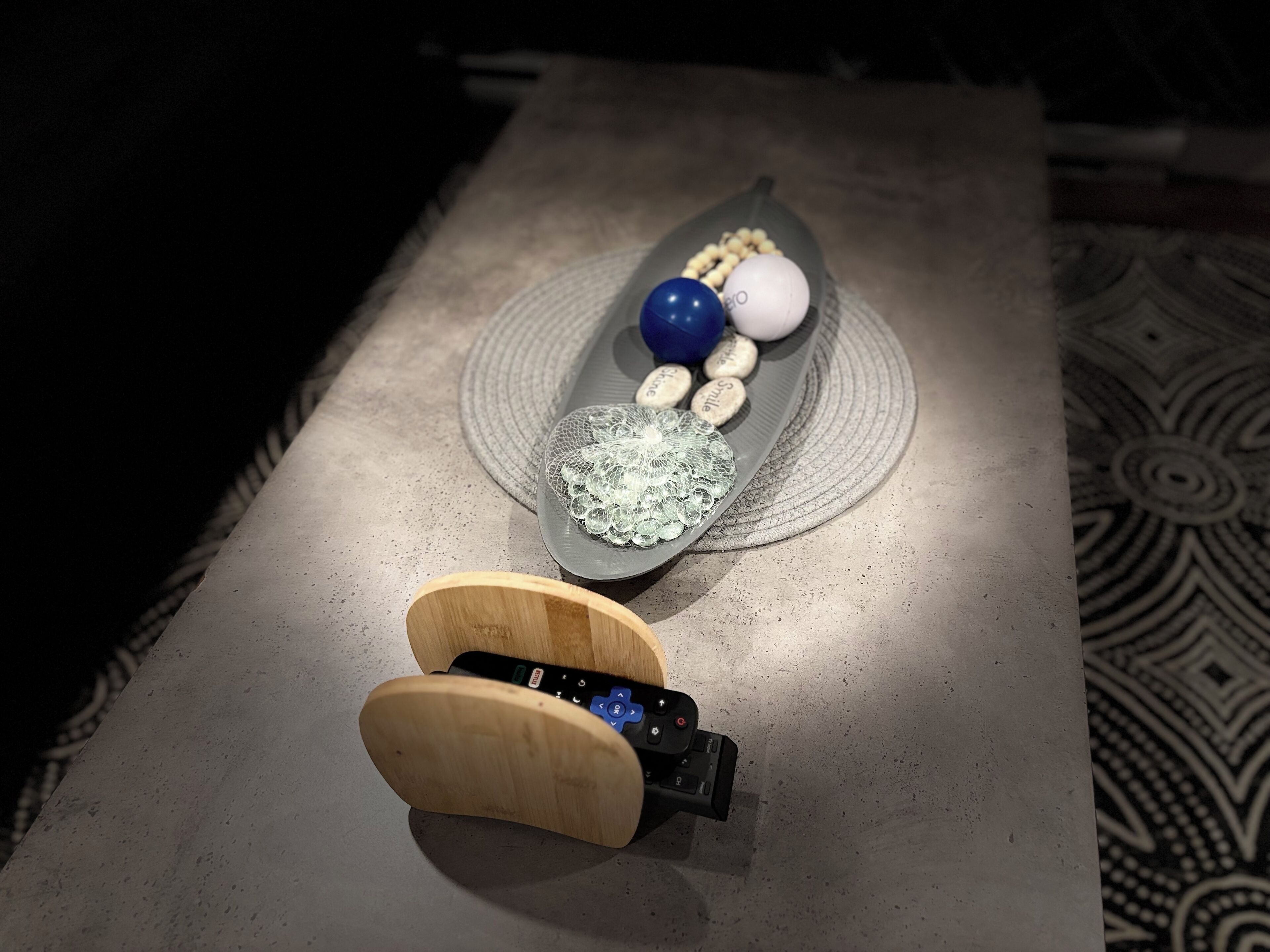 A table with a wooden object, a glass container with beads, and a patterned floor.