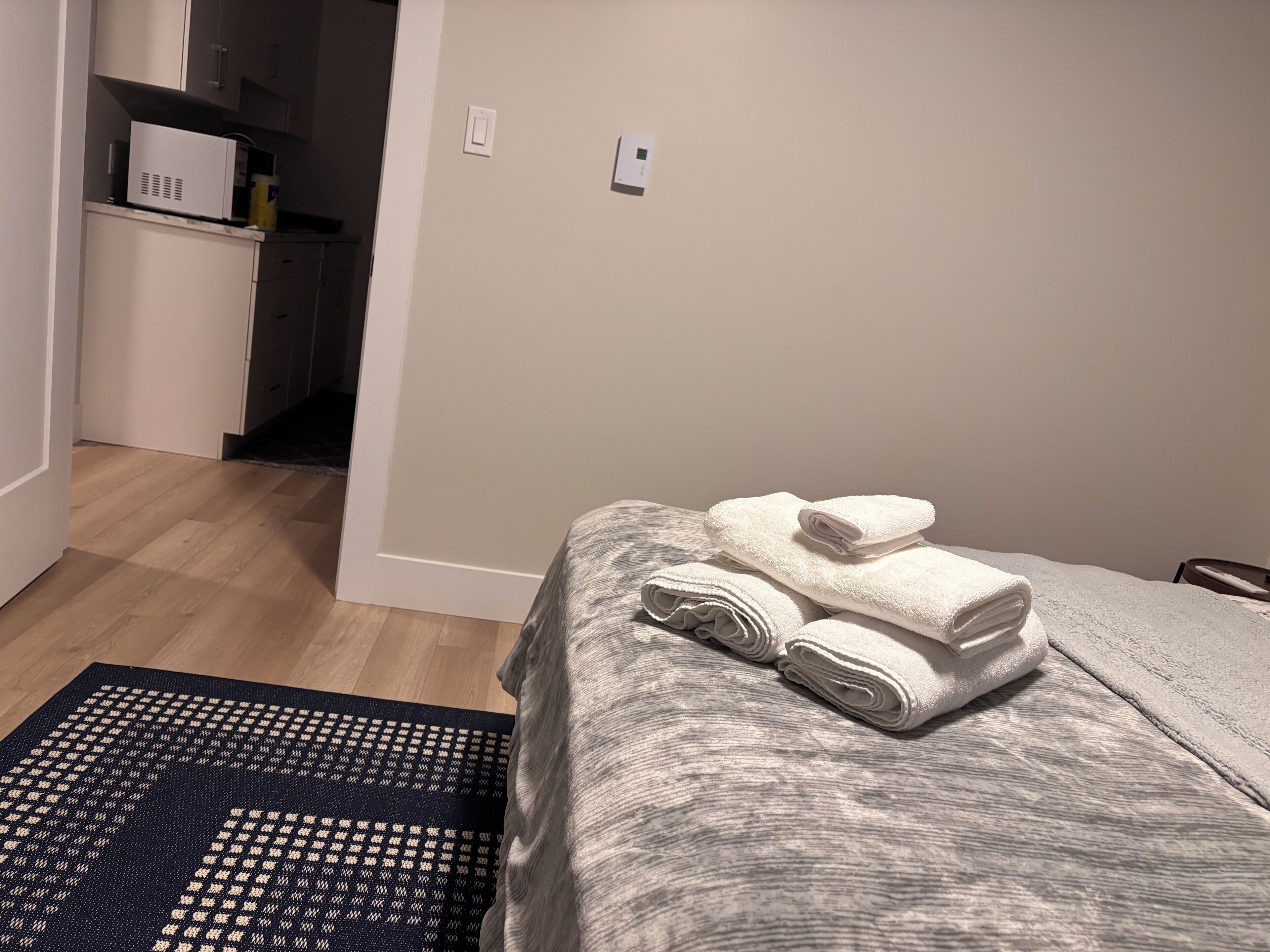 Hotellihuone, jossa on sänky, pieni työpöytä ja tummakuvioinen matto.
