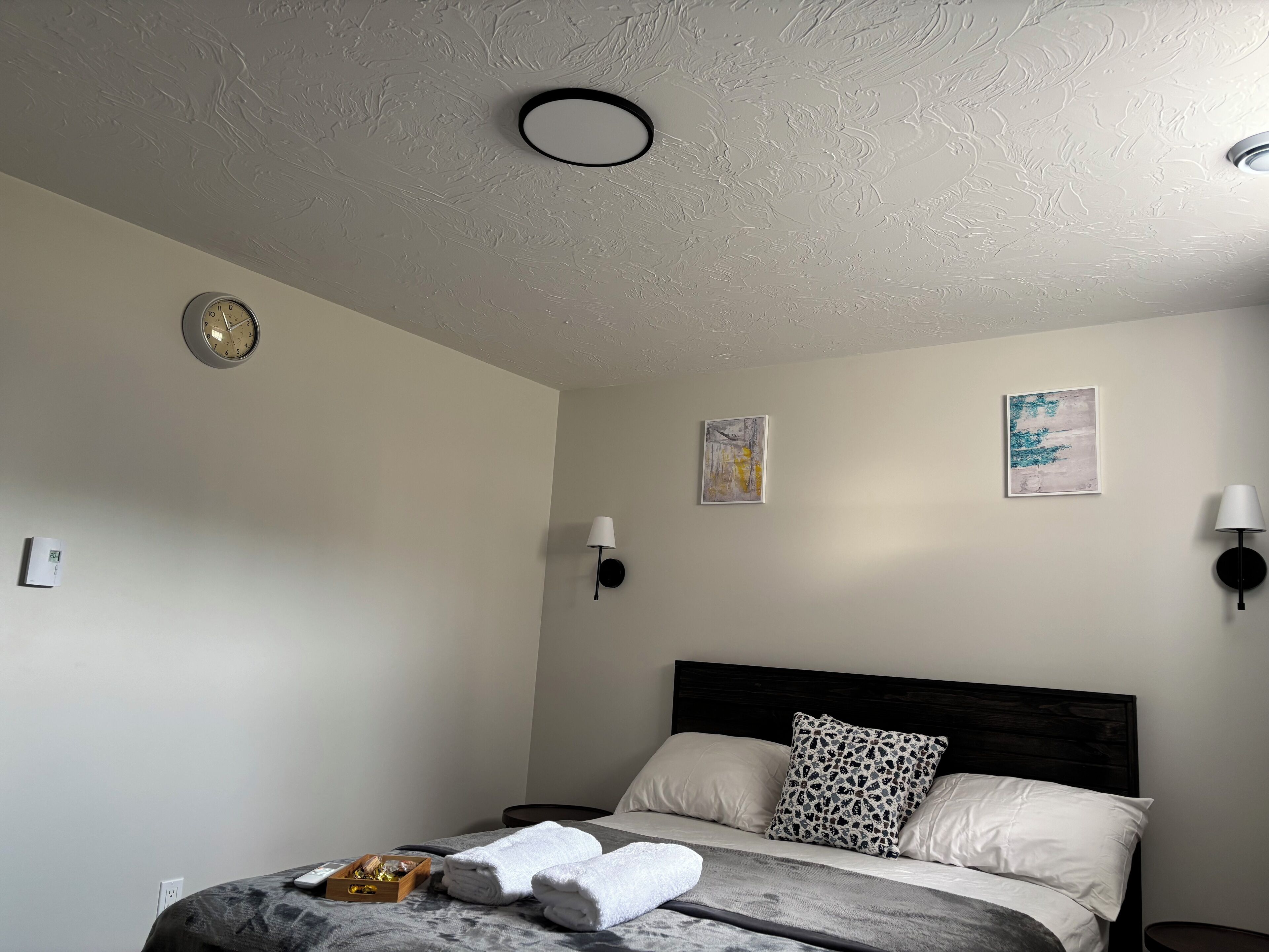 Een slaapkamer met een bed, een wandklok, twee wandlampen en twee ingelijste foto's.