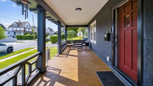 A covered porch with a red door, outdoor furniture, and a view of the street. - 16 Guest, 10 Bed, Family Getaway- 30 min from NYC (New Rochelle)