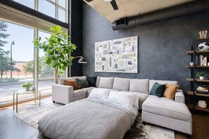 Un salon moderne avec un canapé d’angle, une grande fenêtre et une œuvre d’art abstraite accrochée au mur.