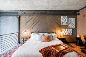 A modern bedroom with a large bed, wooden flooring, and a view of the outdoors.