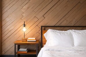 En pænt redt seng med hvide sengetøj, et natbord med en lampe og en stak bøger.