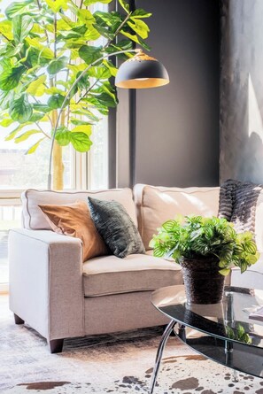 Un salon moderne avec un canapé, une table basse en verre, une plante en pot et une suspension.