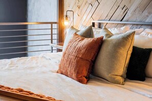 A neatly made bed with a white comforter and several pillows, a wooden headboard, and a metal railing. - Obsidian City View, Sky Lounge, Sauna, RL Therapy (Charlotte)