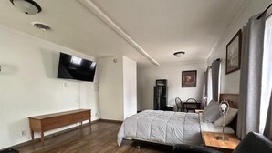 Een hotelkamer met een bed, een bureau, een stoel, een aan de muur bevestigde televisie en een koelkast.
