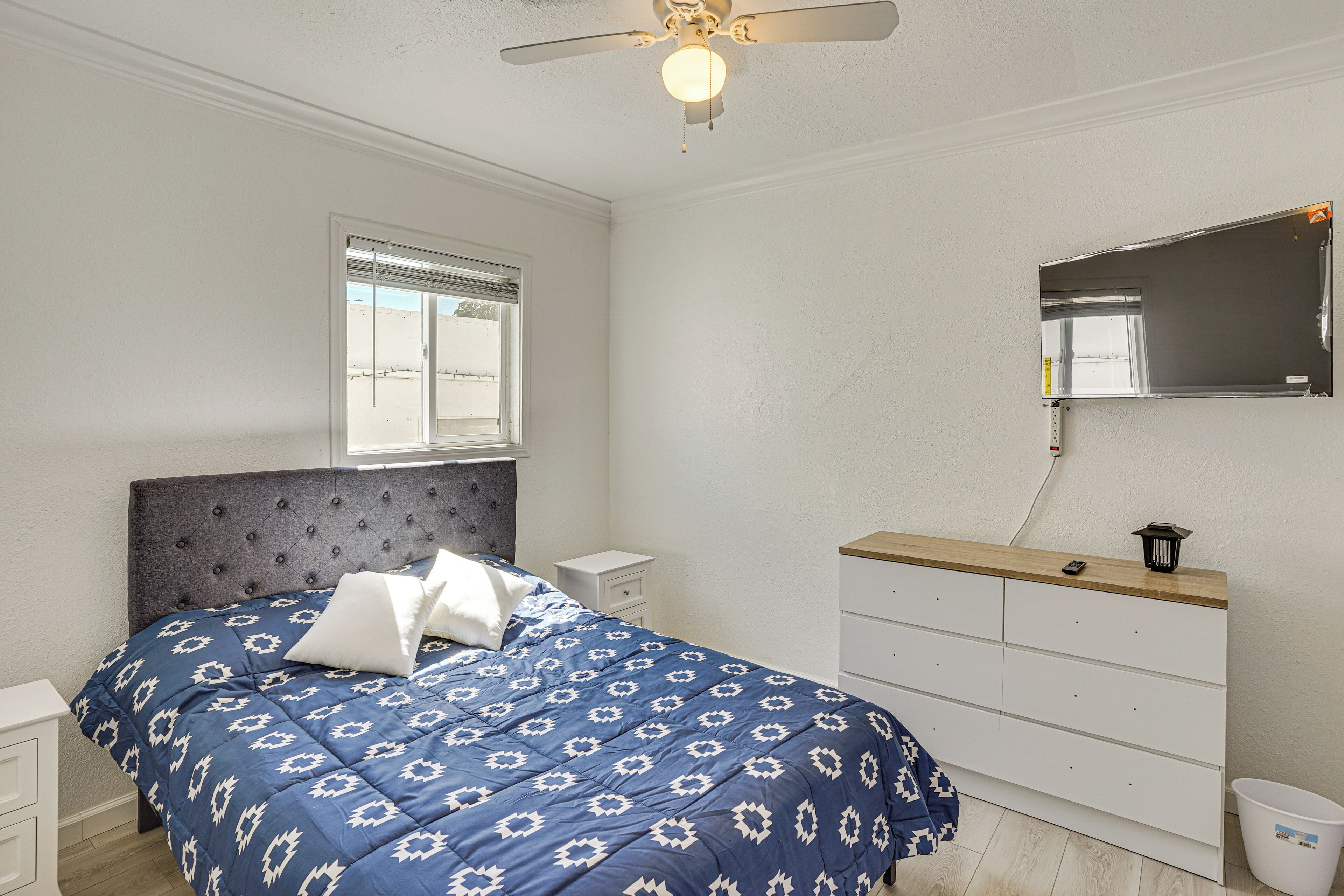 A bedroom with a bed, bedside tables, a dresser, a ceiling fan, a window, and a mirror.