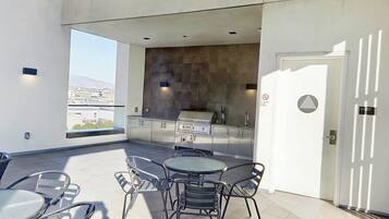 A rooftop patio with a round table and chairs, a built-in grill, and a view of the city.