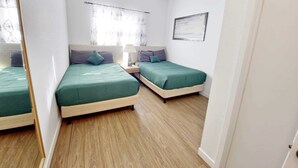 A bedroom with two beds, a nightstand, a mirror, and a window with curtains.