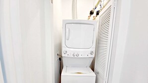 A compact, white laundry room with a front-loading washing machine and dryer, a visible power outlet, and a vented dryer on the right.