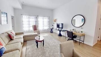 A modern living room with a sofa, armchairs, a coffee table, a desk with a computer, and a large mirror.