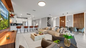 A modern living room with a sectional sofa, a coffee table, and a dining area with chairs. -  9BR Luxury Disney Villa Best Location @ Storey Lake Pool, Theater Sleeps 20 (Kissimmee)