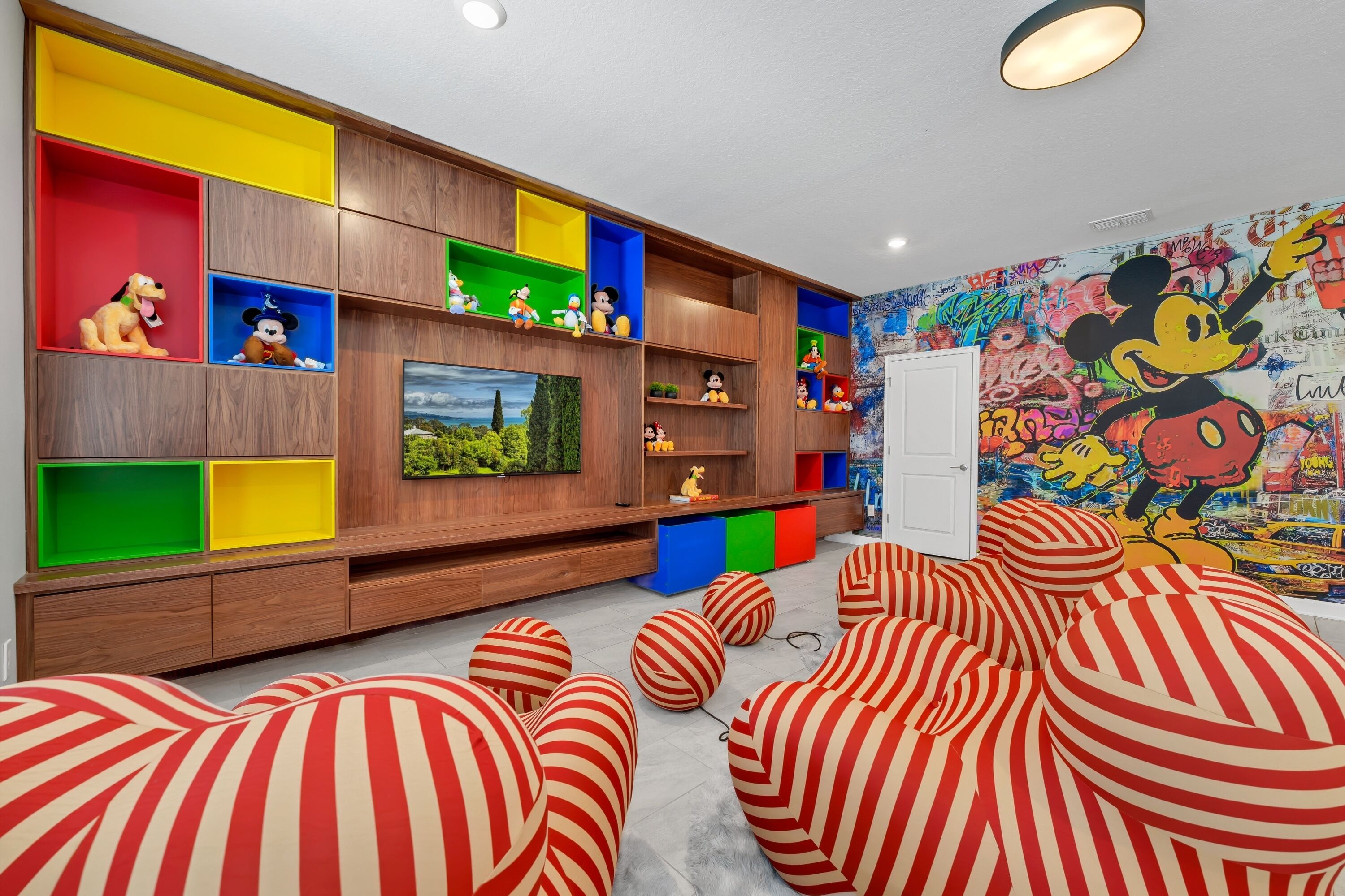 A modern living room with a wooden entertainment unit, colorful storage compartments, and a large Mickey Mouse mural on the wall.