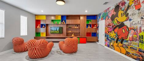 A modern living room with a colorful entertainment unit, a large Mickey Mouse mural, and striped ottomans.