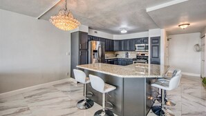 Una cocina moderna con armarios oscuros, electrodomésticos de acero inoxidable y una isla central con taburetes de bar.