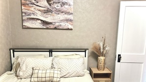 Un dormitorio con cama, almohadas, una mesita de noche, un florero y una puerta.