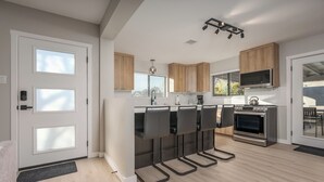 A modern kitchen with wooden cabinets, a central island with bar stools, a built-in oven, and a large window with blinds. - The Desert Rose A Modern home in a great location (Sedona)