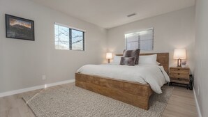 A bedroom with a wooden bed, two bedside tables with lamps, a large window, and a framed picture on the wall. - The Desert Rose A Modern home in a great location (Sedona)
