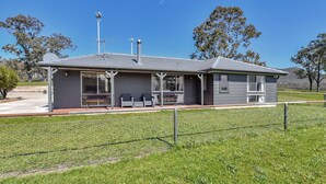 A two-story building with a flat roof, a fenced outdoor seating area with benches, and a clear blue sky in the background. - Andres Farm Cottage (Broke)
