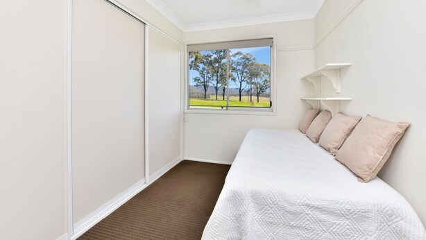 A bedroom with a bed, a window with a view of trees, a ceiling fan, and a sliding door. - Andres Farm Cottage (Broke)