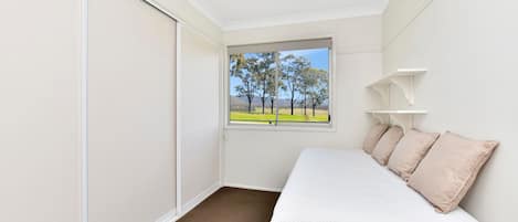 Un dormitorio con cama, ventana con vista a árboles, ventilador de techo y puerta corredera.