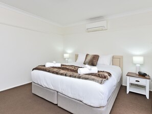 Una habitación de hotel con cama, mesitas de noche y un equipo de aire acondicionado.