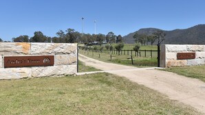 A stone gate with a sign reading 'Andre's Farm' leading to a rural landscape with a dirt path, trees, and a hill in the background. - Andres Farm Cottage (Broke)