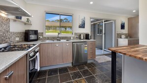 A modern kitchen with a gas stove, dishwasher, and a large window. - Andres Farm Cottage (Broke)