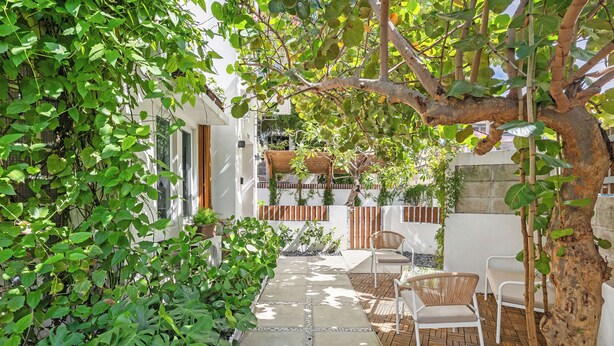 Une terrasse avec un sol en pierre, des chaises blanches et un arbre.
