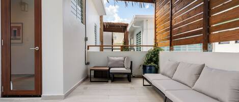 Un balcón con una pérgola de madera, un sofá, una mesita y una silla.