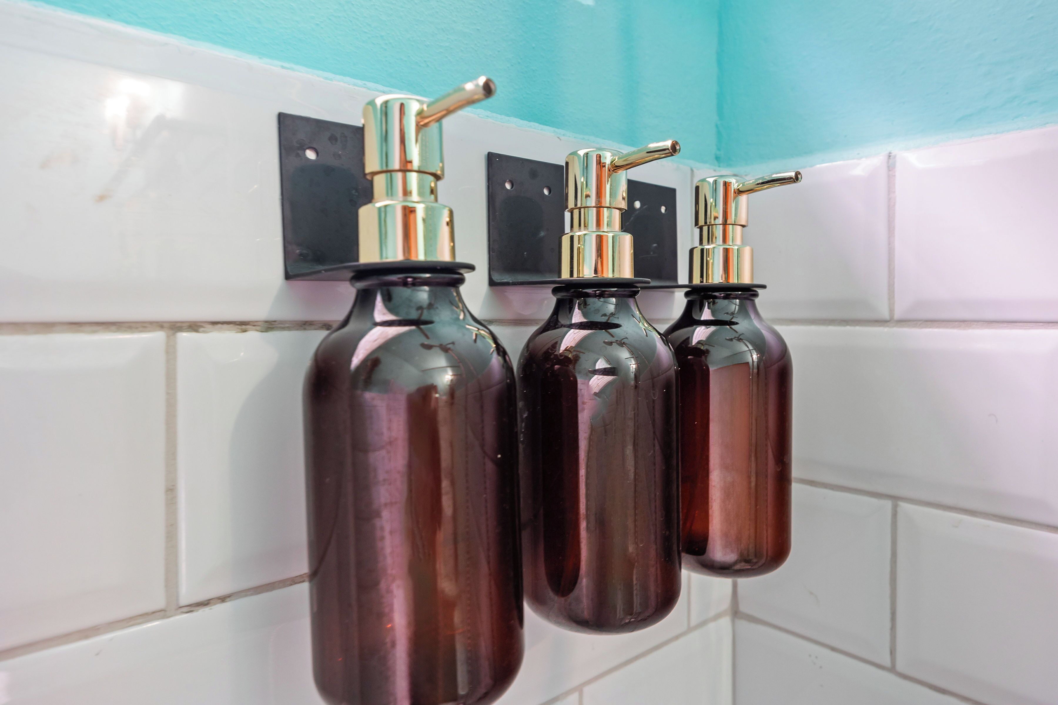 Three dark brown bottles with metallic pumps mounted on a tiled wall.