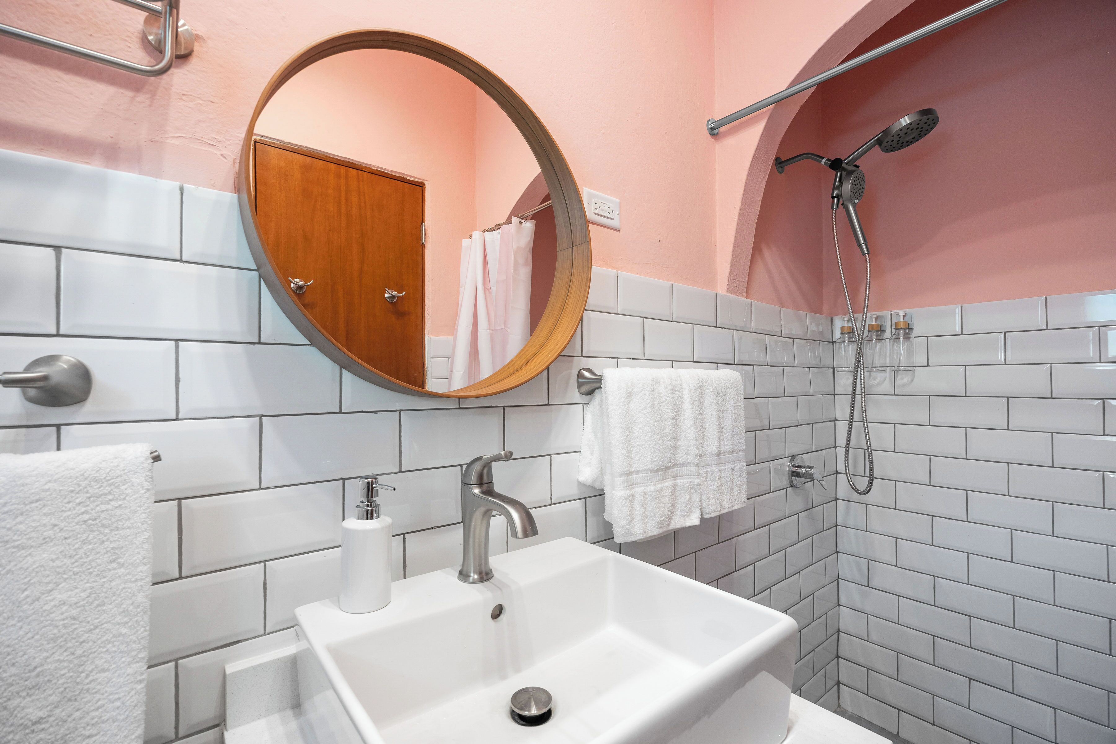 A bathroom with a white sink, a round mirror, a shower, and a towel rack.