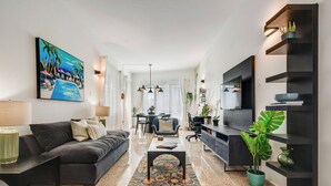 Un salon moderne avec un canapé foncé, une table basse et un téléviseur posé sur un meuble noir. Un tableau orne le mur et une plante est placée sur le sol.