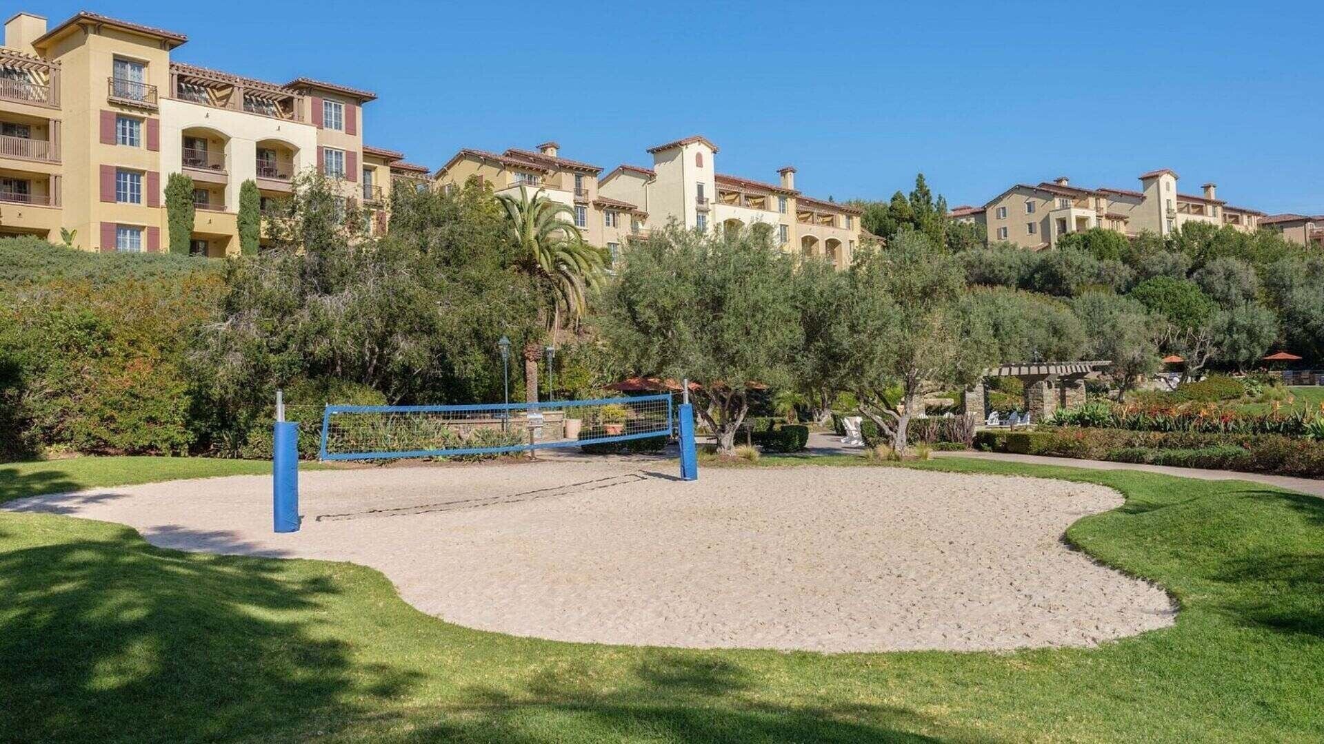 A courtyard with a volleyball net, surrounded by greenery and buildings with balconies.