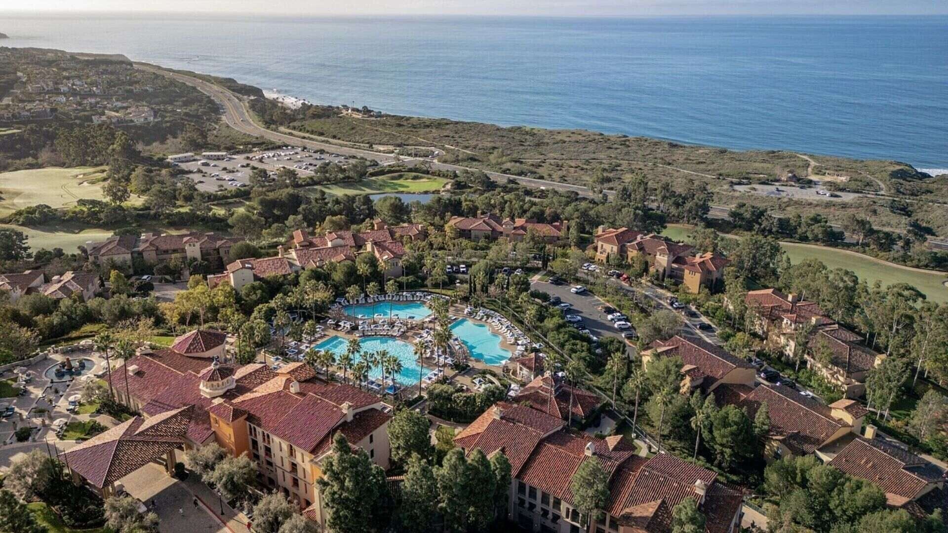 Un complexe hôtelier doté d’une piscine centrale, entouré de villas, d’un parcours de golf et offrant une vue sur l’océan.