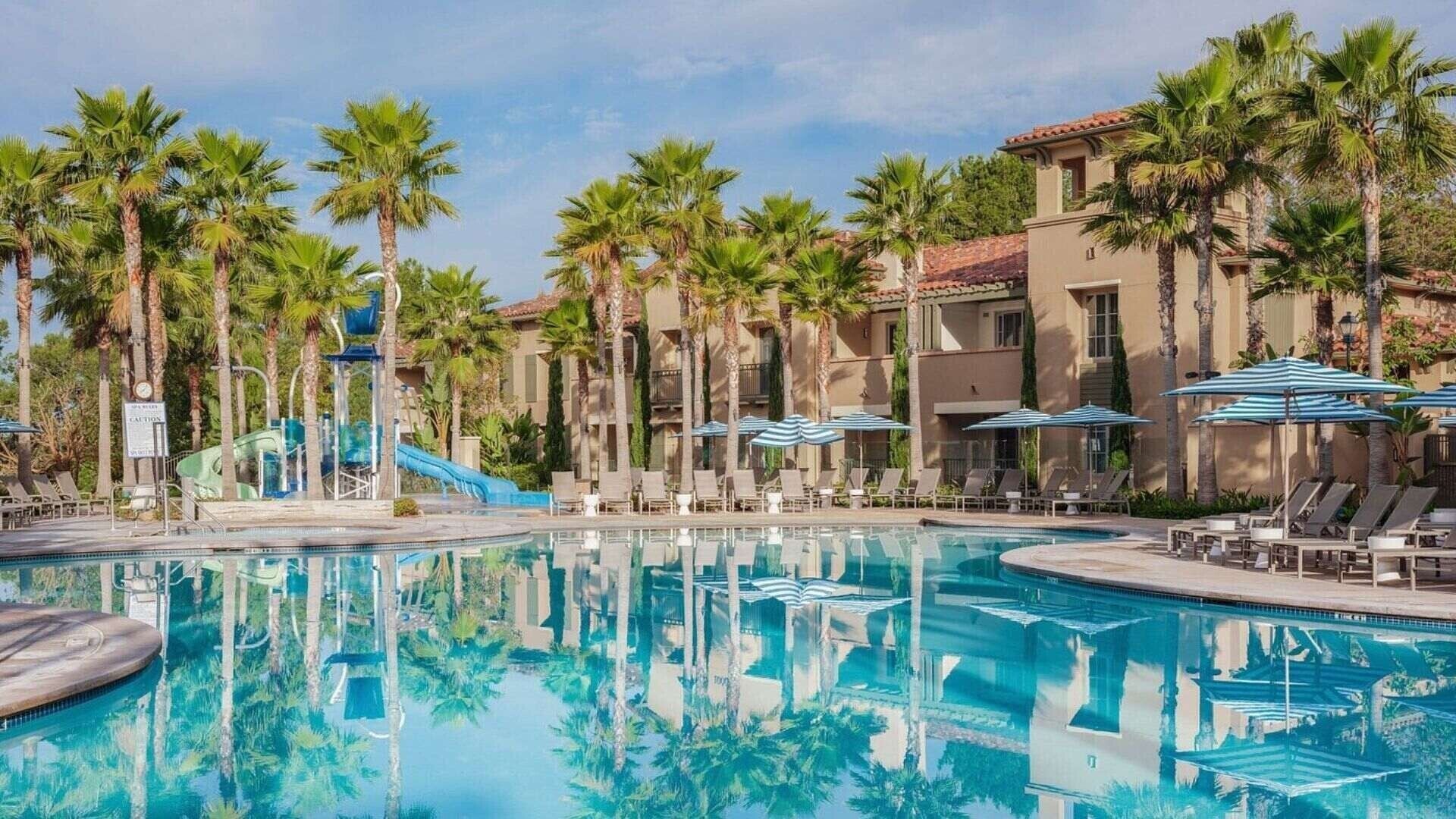 Un espace piscine doté de chaises longues, de palmiers et d’un toboggan aquatique.