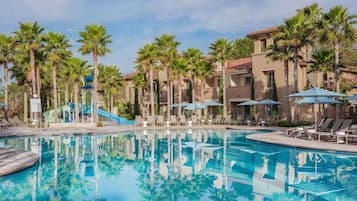 Un espace piscine doté de chaises longues, de palmiers et d’un toboggan aquatique.