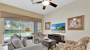 Un salon comprenant un canapé, un fauteuil, une table basse, un téléviseur et un ventilateur de plafond.