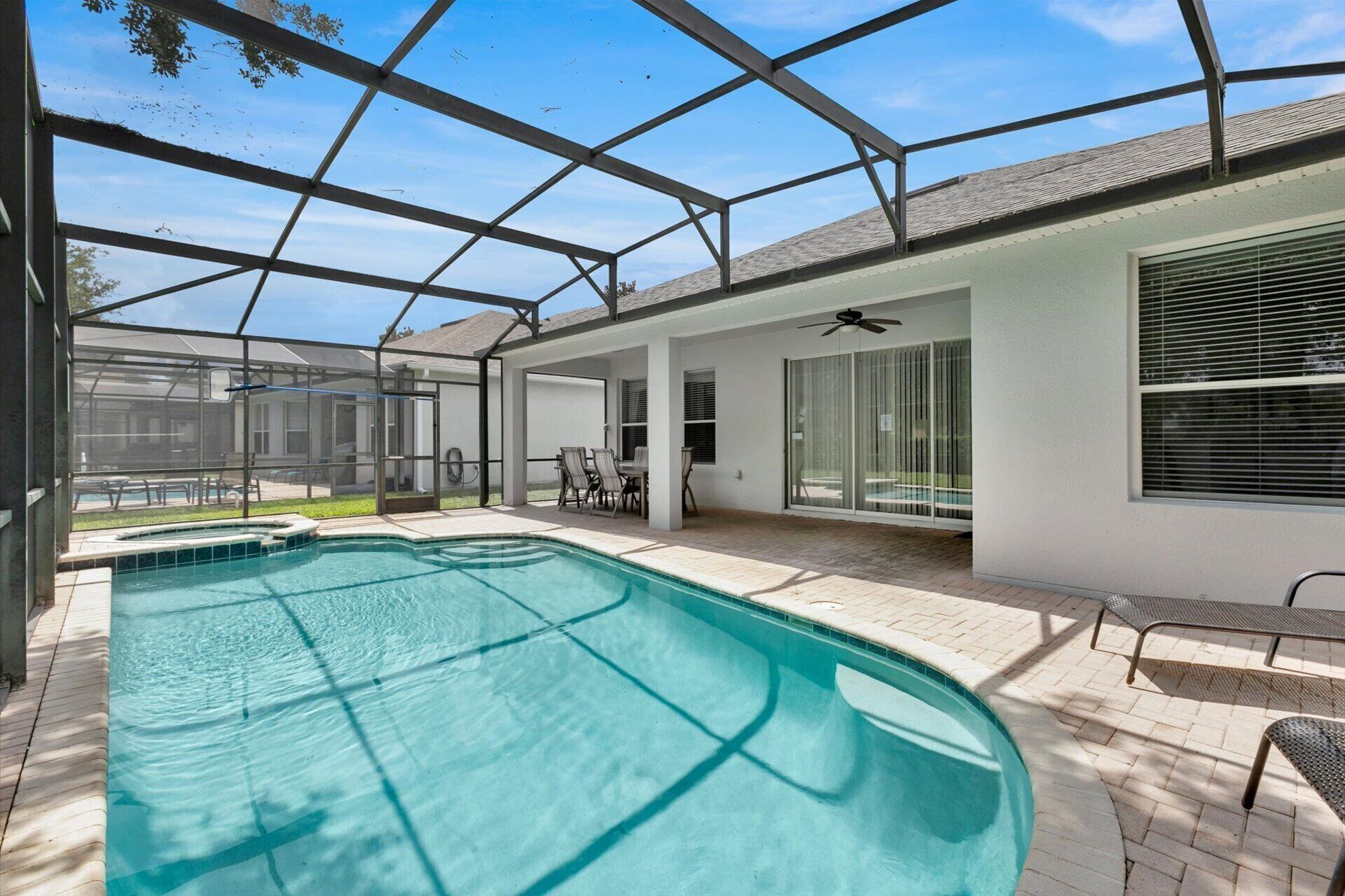 Ein überdachter Pool mit Glasdach, Terrassenmöbeln und Deckenventilator.