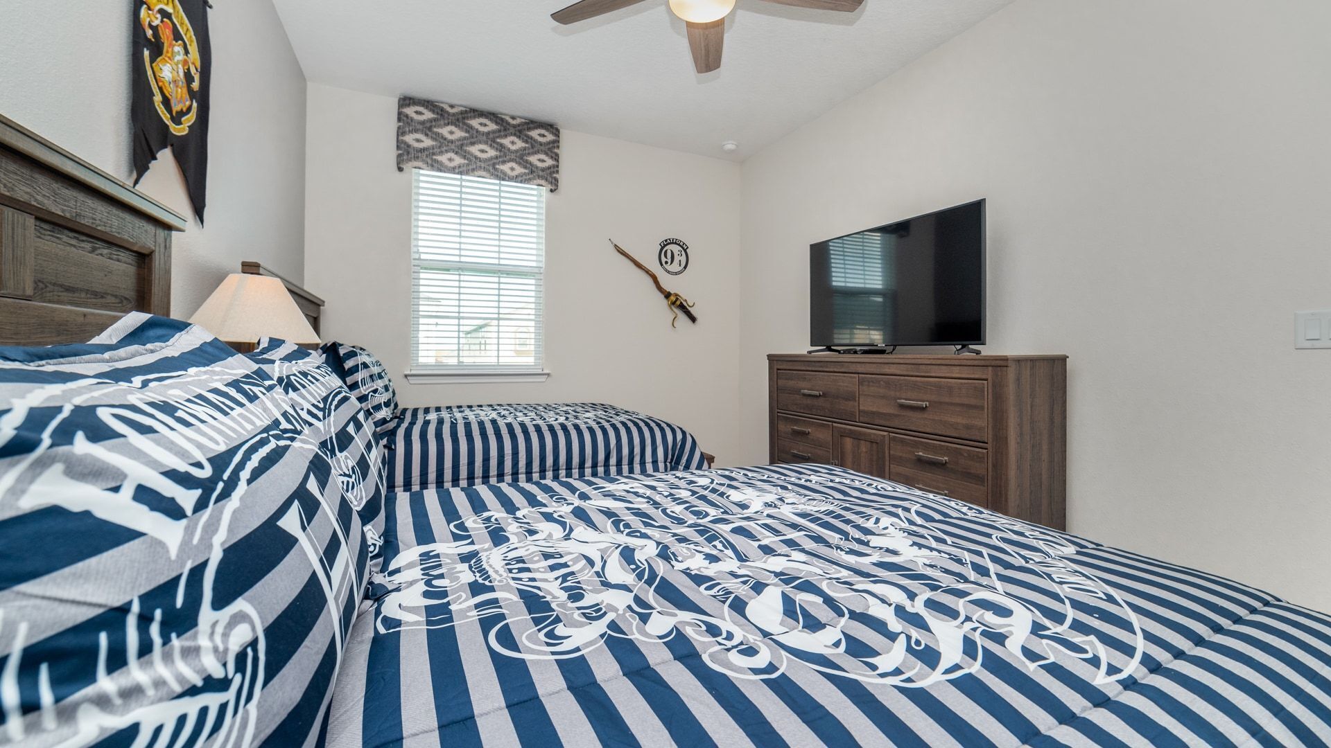 A bedroom with a bed, a dresser, a television, and a window with blinds.